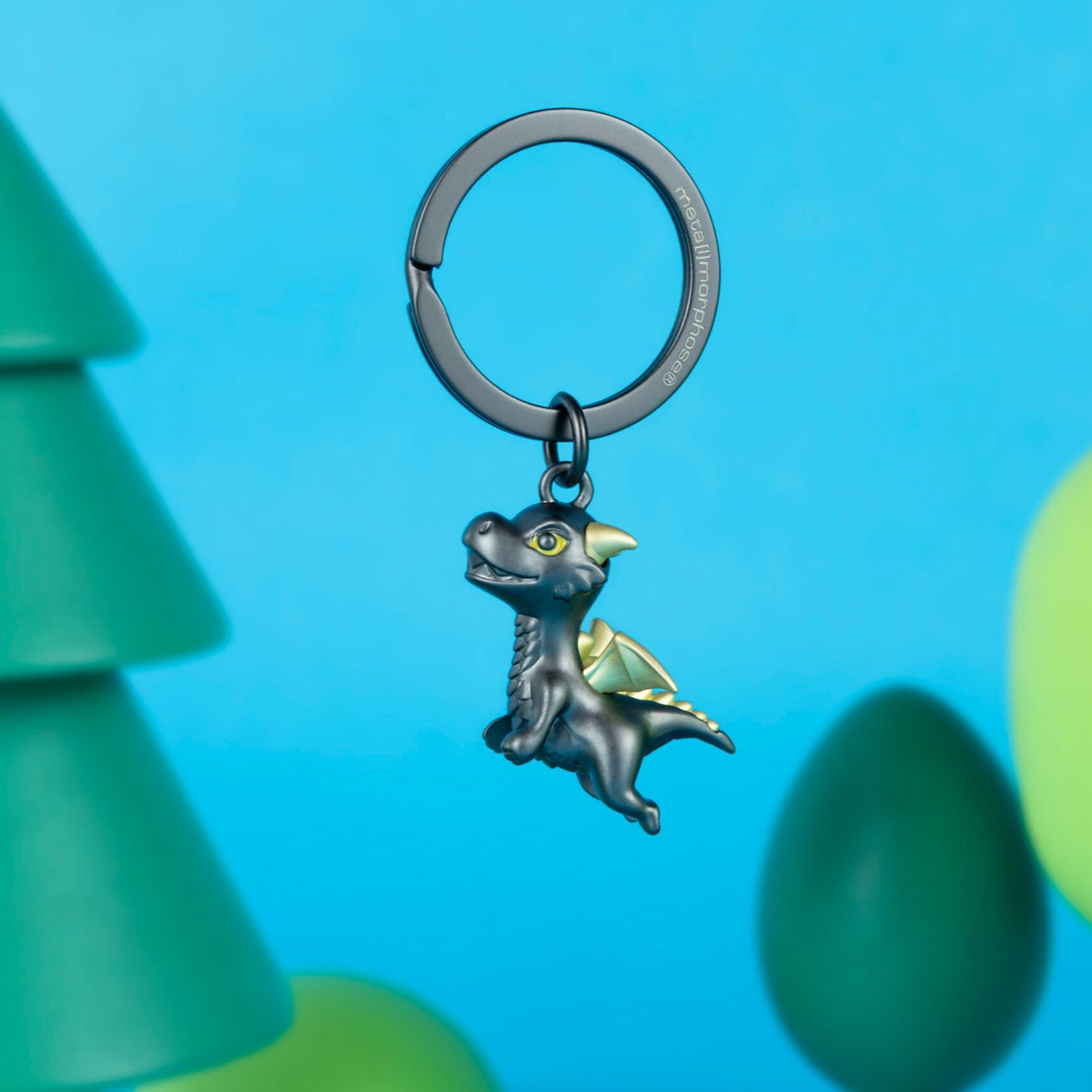 Keychain with a dinosaur design against a blue background with green tree-like shapes.